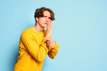Portrait of young man with curly hair posing, whispering secret information isolated over blue background