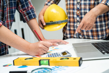 Asian engineer and partner team learn and talk with house plan project blueprint, graph and yellow helmet and engineering construction tools on table work.