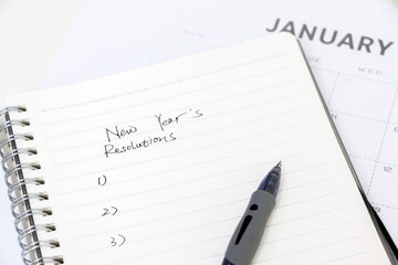 Writing new year’s resolutions, list on notepad with ballpoint pen, January calendar in...