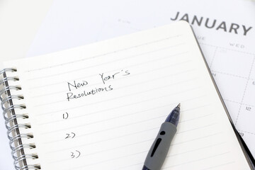 Writing new year&rsquo;s resolutions, list on notepad with ballpoint pen, January calendar in background, selective focus. Setting goals for the new year.