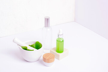 Mortar and pestle with fresh green ginkgo leaves, cosmetic serum and tonic bottles, cream jar on...