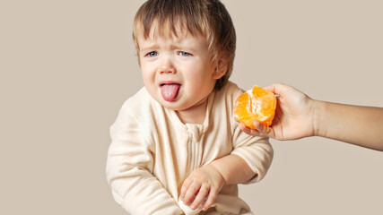 a baby, child with a food allergy doesn't want to eat sour orange, winces, the baby refused to eat...