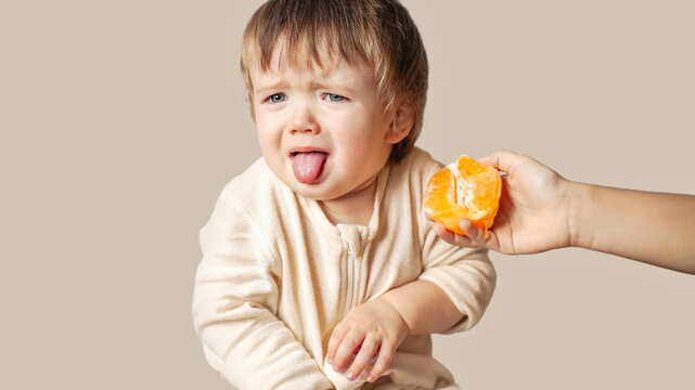 A Baby, Child With A Food Allergy Doesn't Want To Eat Sour Orange, Winces, The Baby Refused To Eat Vitamins , He Made A Grimace And Stick Out His Tongue