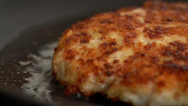 Macro shot of fried chicken schnitzel in sizzling oil in hot frying pan. Chicken meat is fried on stove. Food concept