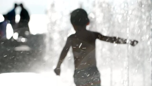 Blurred Shot Of Little Boy Playing In Water Park Jets In City During Hot Summer Day In Super Slow Motion 120fps