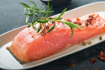 Salmon fish piece. Fresh raw salmon fish piece on marble board stand with herbs and lemon on black background. Seafood or menu concept. Top view.