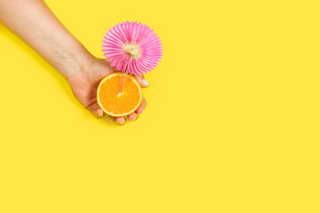 Mano de mujer sosteniendo una rodaja de naranja sobre un fondo amarillo liso y aislado. Vista...