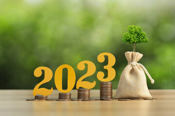  Text of 2023 on top of coins stacks with a sack and small plant tree. 2023 New year saving money...