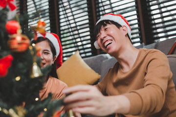 Group of happy Asian friends celebrating Christmas and decorate the Christmas tree indoors. Beauty woman with Christmas Gifts. New Year party. Woman hands decorate Christmas tree red ball, bauble.