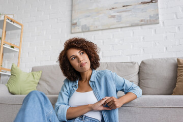 dreamy african american woman sitting near modern sofa in living room.