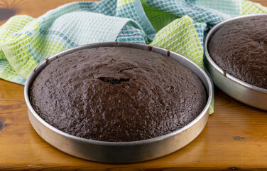 Unfrosted chocolate cakes in pans on wooden table