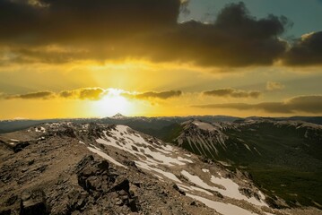 View of the rocky mountain range against the background of the cloudy sky at sunset.