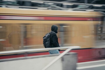 Person in a black hooded jacket and backpack walking near a moving train