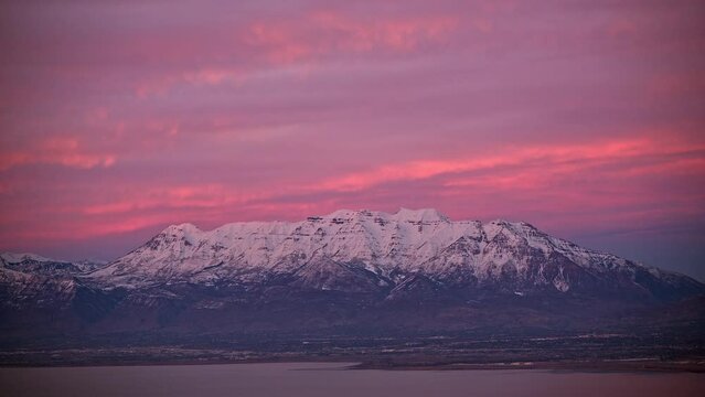 Timelapse of sunset lighting up snow capped mountain and sky over Utah Valley.