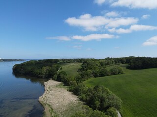 Fototapeta premium Aerial view of a calm river with green trees and a cloudy blue sky