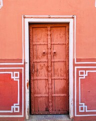 Old wooden door painted red on a red building with white ornaments