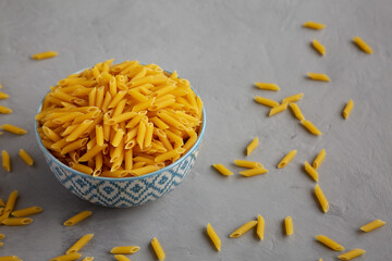 Homemade Raw Dry Mini Penne Pasta in a Bowl on a gray background, side view.