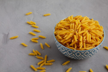 Homemade Raw Dry Mini Penne Pasta in a Bowl on a gray background, side view.