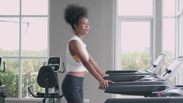 Side view of Fitness girl running, jogging with cardio training on track treadmill. Black woman with muscular bodycare in exercise gym sport club. Fitness, exercising and healthy lifestyle Concept.