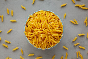 Homemade Raw Dry Mini Penne Pasta in a Bowl on a gray surface, top view. Flat lay, overhead, from above.