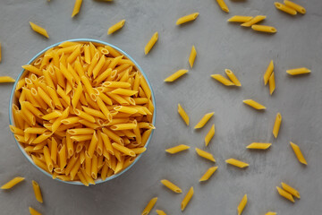 Homemade Raw Dry Mini Penne Pasta in a Bowl on a gray background, top view. Flat lay, overhead, from above.