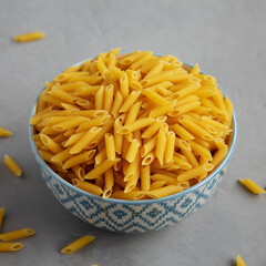 Homemade Raw Dry Mini Penne Pasta in a Bowl on a gray background, side view. Close-up.