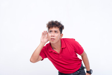 A man in his 20s eavesdropping on a conversation, with his hand placed near his ear. Copy space on...