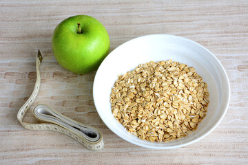 oat flakes in the bowl with green apple and metre on beige background - obrazy, fototapety, plakaty