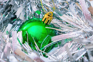 A green Christmas ball lies among the New Year's, fluffy and silver tinsel