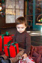 Fototapeta na wymiar Cute toddler boy with red Christmas present at home close-up. New Year's comfort at home.