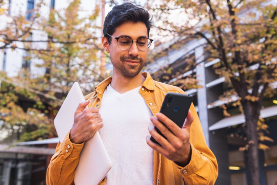 Smiling ethnic man using smartphone on street