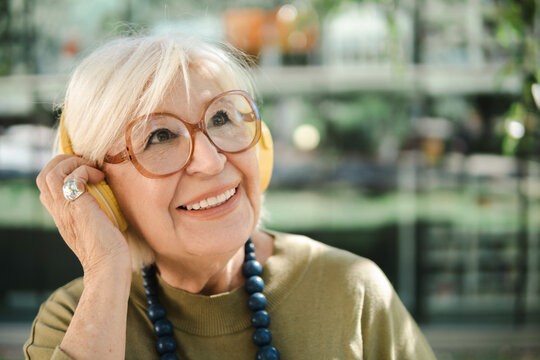 Dreamy aged woman listening to music in earphones