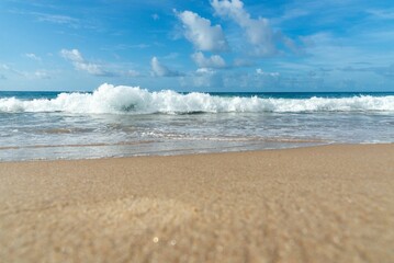 View of sandy beach with foamy waves against blue sky with clouds in background. Barra beach, Brazil