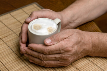A cup of fresh coffee with cappuccino foam in the hands of a man close-up