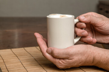A cup of fresh coffee with cappuccino foam in the hands of a man close-up