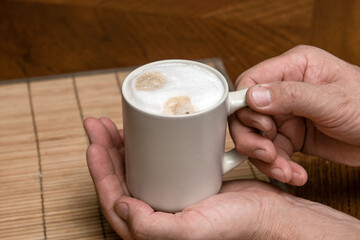 A cup of fresh coffee with cappuccino foam in the hands of a man close-up