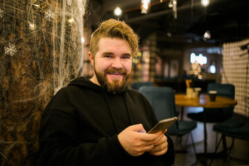 Portrait happy guy making money transaction via application on mobile phone with 4g internet sitting at cafe in street evening, serious millennial man reading text message on smartphone