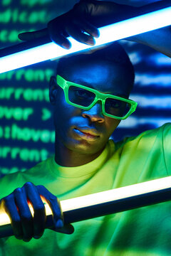 Cool trendy black man in sunglasses touching neon lamps in disco club