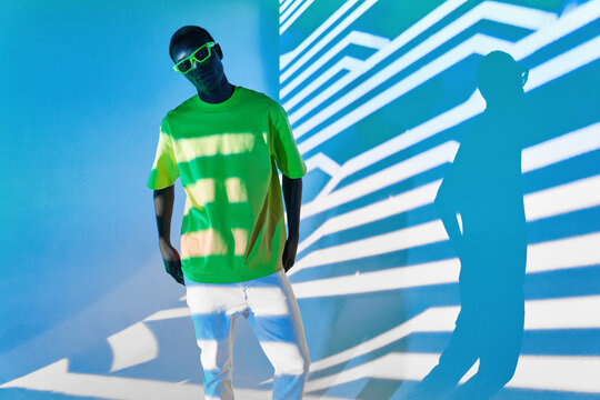 Cool black man in green T shirt and sunglasses posing in shadows