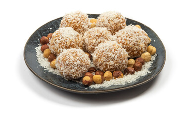 homemade coconut candies with almonds inside, sprinkled with coconut chips, lying on a round plate of dark blue color, decorated with hazelnuts isolate