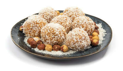 homemade coconut candies with almonds inside, sprinkled with coconut chips, lying on a round plate of dark blue color, decorated with hazelnuts isolate
