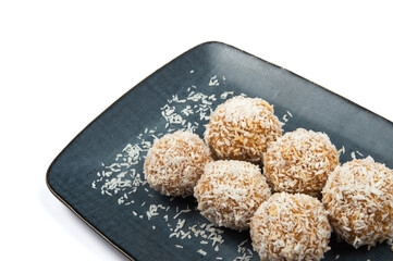 homemade coconut candies with almonds inside, sprinkled with coconut chips, lying on a rectangular plate of dark blue color, decorated with almonds on a white background