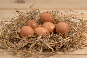 Chicken eggs in straw nest on wood table.