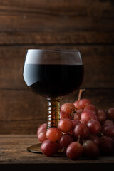 Glass of red wine with red grapes nearby, dark rustic background