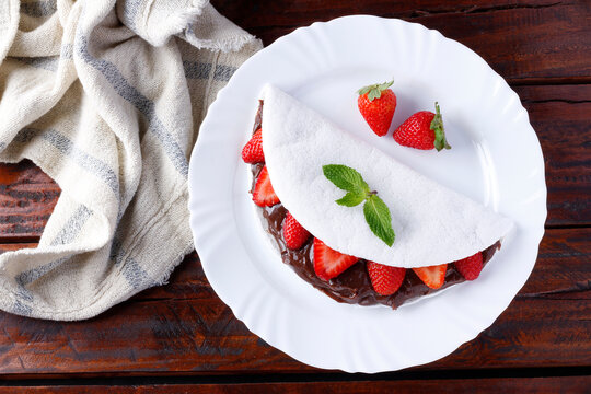 homemade tapioca or beiju stuffed with strawberry and chocolate on white plate over rustic wooden table