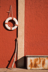 Aufnahme einer roten Wand mit einem Rettungsring und einer rostigen Kiste