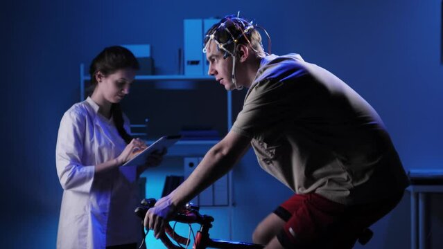 EEG topographer for examining brain, doctor making electrogram of scalp activity. Researching of brain work, man riding bicycle in electroencephalography headset. Rehabilitation after damage in sport.