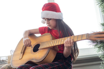 Child playing the guitar and singing near a christmas tree