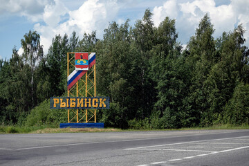 Stella at the entrance at the edge of the road with the name of the city "Rybinsk" on the background of green foliage. landmark Rybinsk