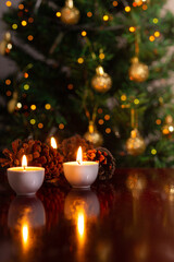 Decoração de Natal. Algumas velas acesas em uma superfície refletiva e um detalhe desfocado da árvore de Natal ao fundo.